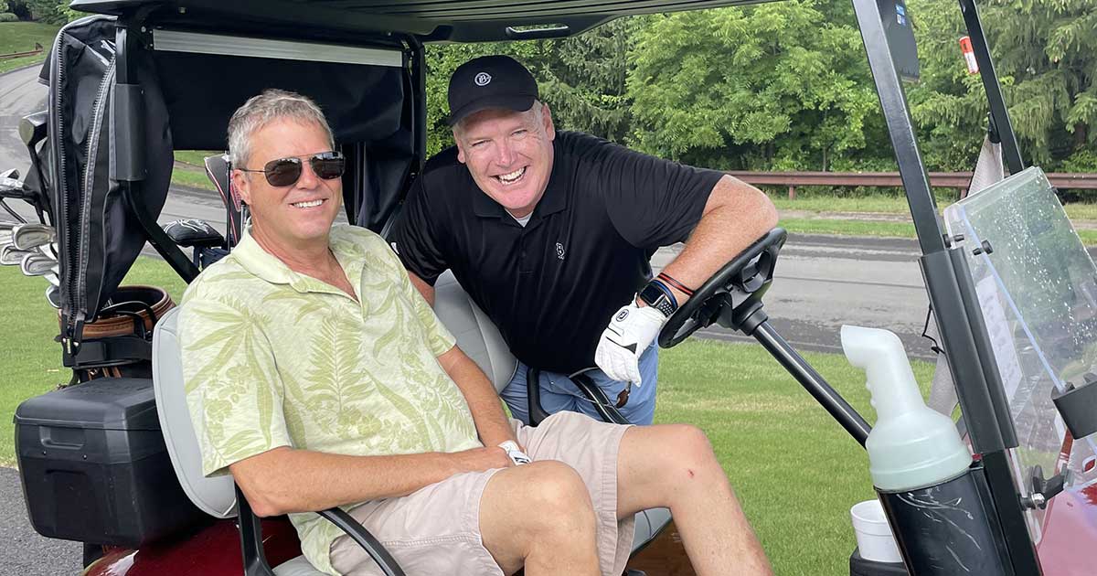 2 men in a golf cart smiling