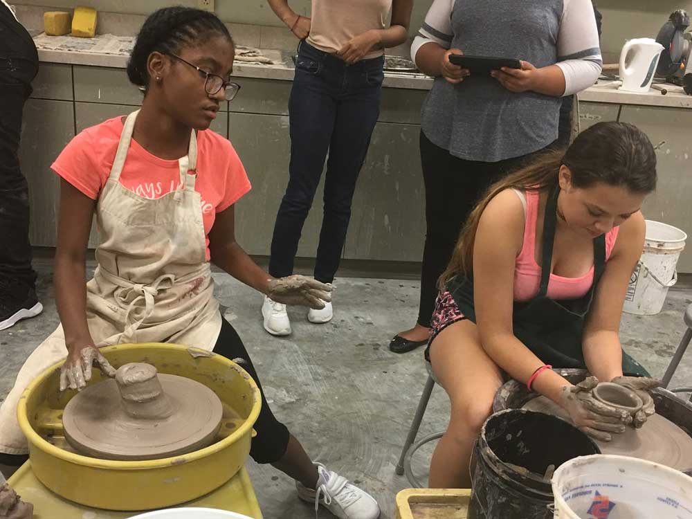 2 students throw clay on a wheel